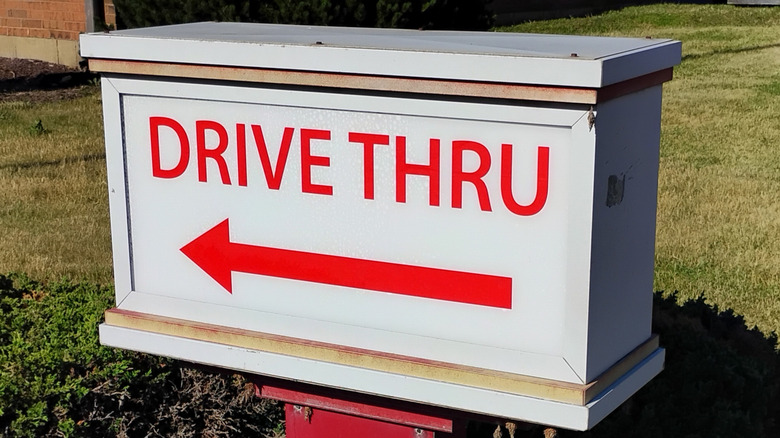 A drive thru sign with red lettering on a white background with the arrow pointing to the left