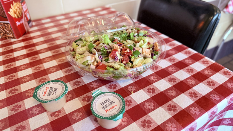 Open Portillo's salad container with two dressing cups on checkered tablecloth