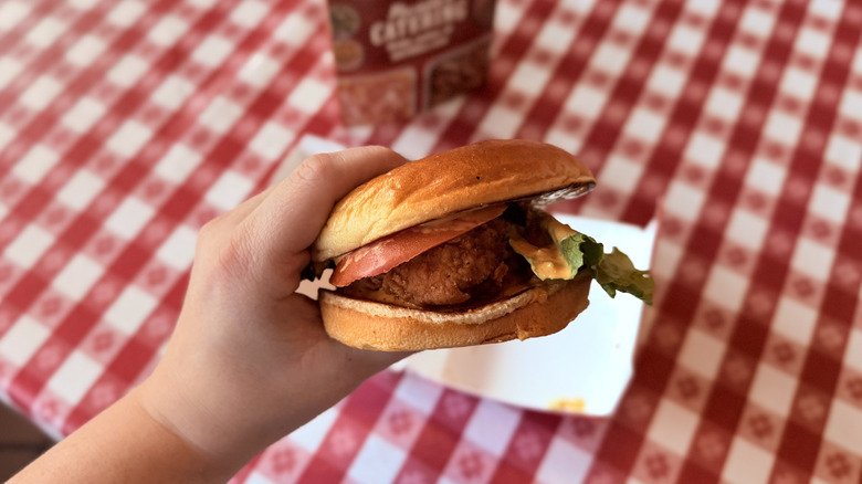 Hand holding a Spicy Chicken Sandwich in front of checkered tablecloth
