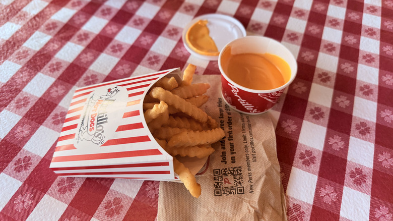 Carton of french fries with cup of cheese sauce on checkered tablecloth