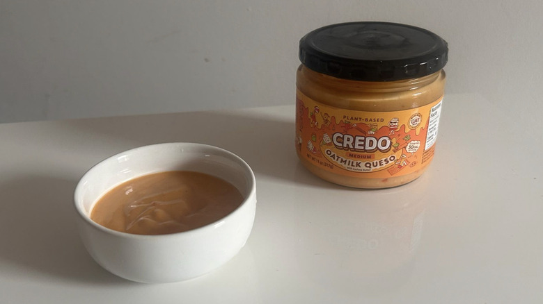 A jar of Credo Oatmilk Queso spooned into a white bowl