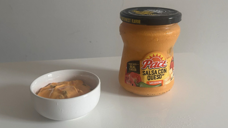 A jar of Pace salsa con queso spooned into a small white bowl