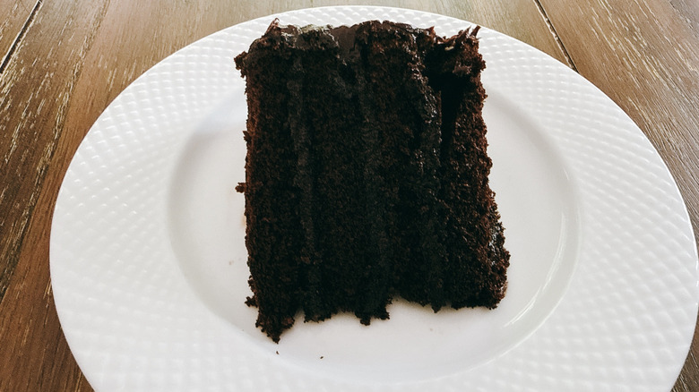 Publix chocolate cake slice with fudge icing on white plate on wooden table