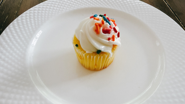 Publix mini vanilla cupcake with sprinkles on white plate on wooden table