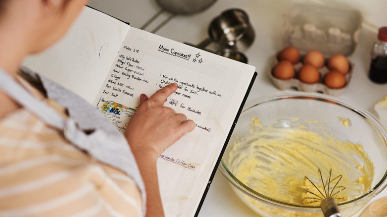 Person looking at a recipe book in the kitchen with ingredients for cupcakes