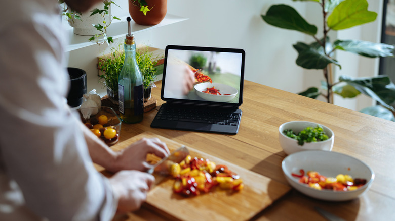 Person watching cooking video on a laptop while chopping vegetables