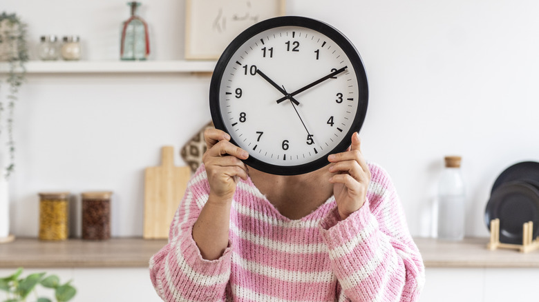 Person hiding their face with a clock in the kitchen