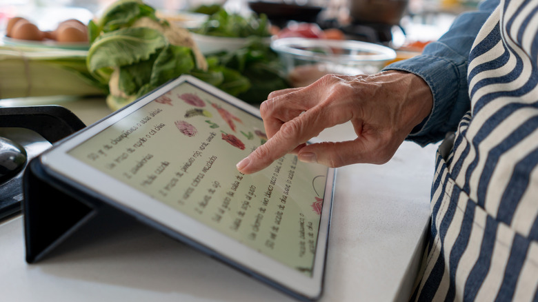 Person following a recipe online on a digital tablet while cooking at home