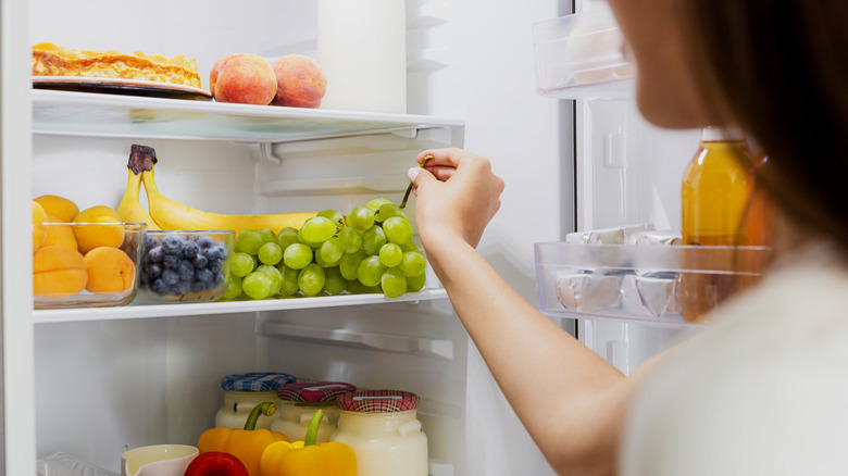 Person taking some grapes from an open fridge