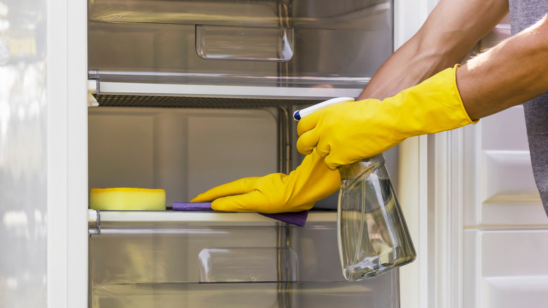 Person in yellow rubber gloves cleaning fridge shelves