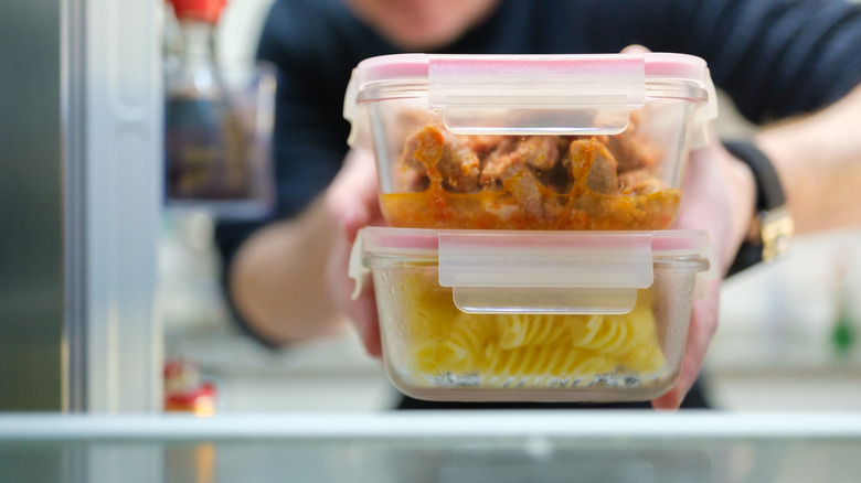 Hands taking boxes of pasta and chicken leftovers from the refrigerator