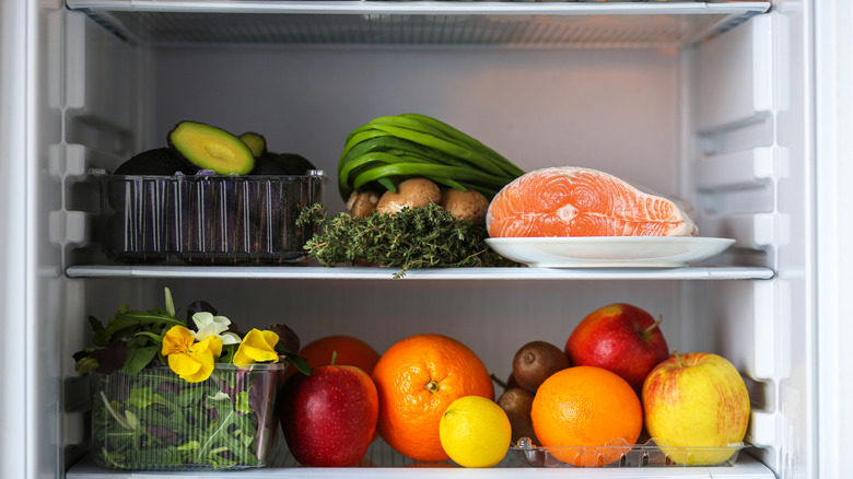 Open fridge with salmon, fruit, and vegetables inside