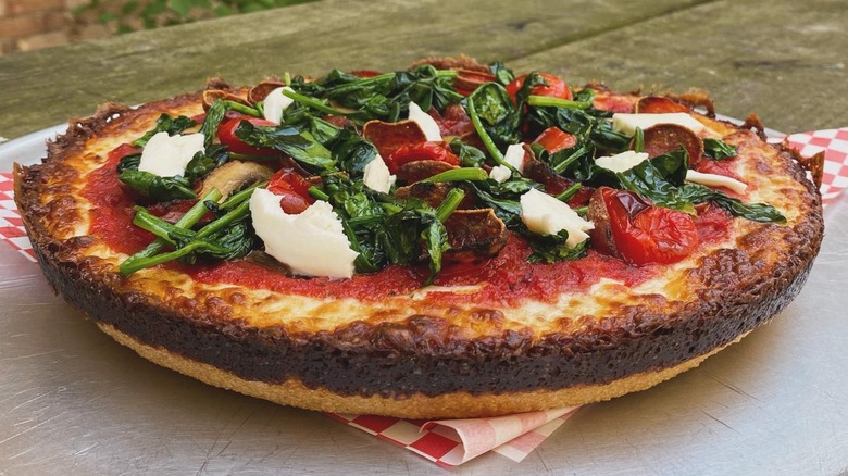A Milly's pan pizza topped with spinach, tomatoes, and fresh mozzarella