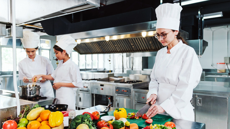 Chef wearing white toque and uniform cutting vegetables on a green cutting.board