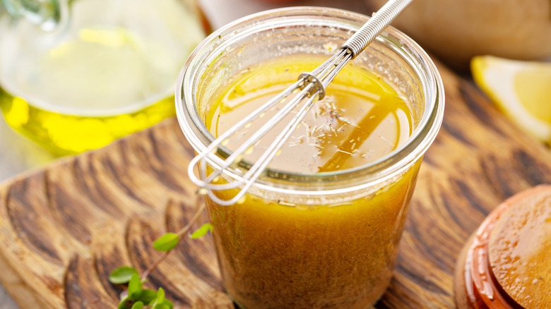 Homemade greek salad dressing or marinade in a glass jar with a tiny whisk