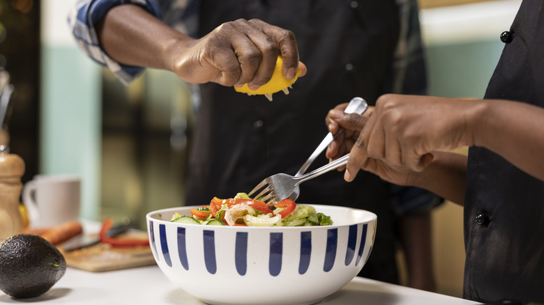 Couple adding lemon juice over salad and mixing goods in decorative bowl