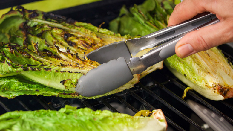 Person flipping grilled romaine lettuce with tongs