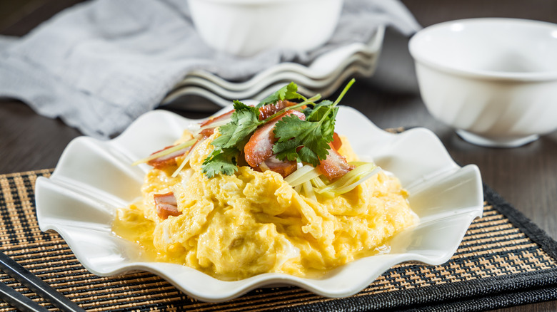Scrambled eggs topped with fresh herbs and crab meat on a fluted white plate