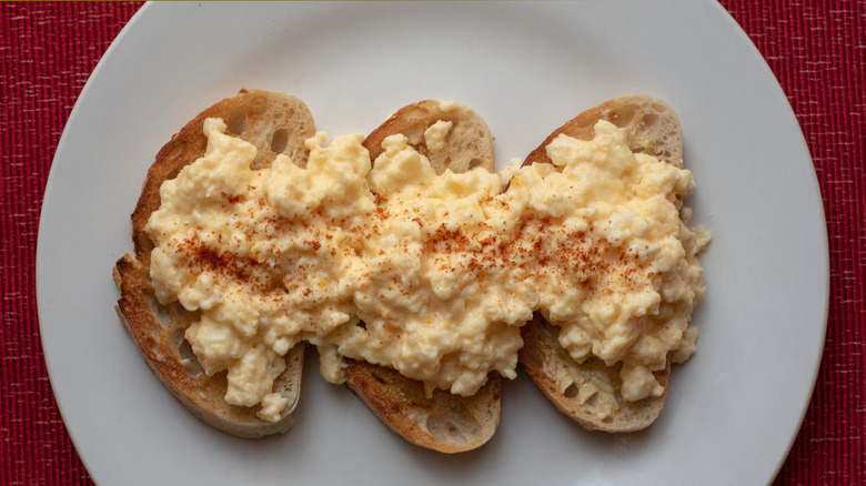 Three pieces of toast topped with scrambled eggs and paprika on a white plate