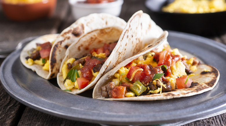 A plate of breakfast tacos, with eggs, beef, cheese and tomato pieces.