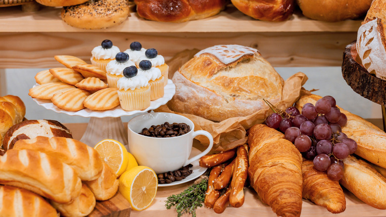 Variety of baked goods including croissants, bread, cupcakes with coffee and grapes on display in bakery.