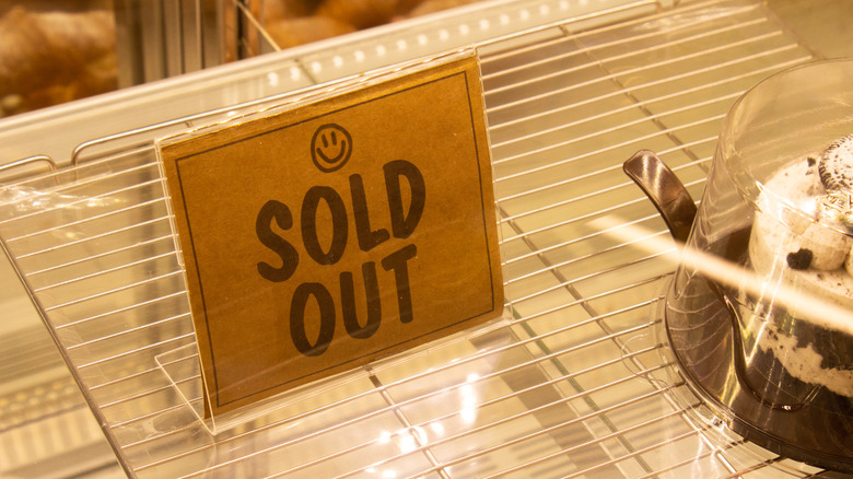 A sold out sign printed on brown paper on the empty rack of a refrigerated case