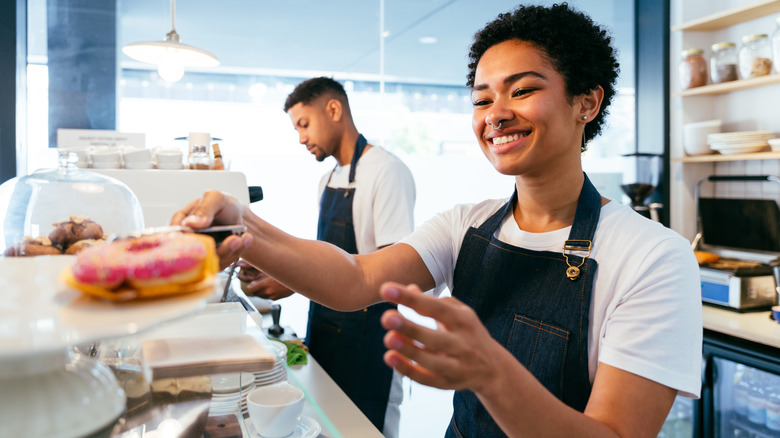 A man and woman working at a cafe behind the pastry case, smiling