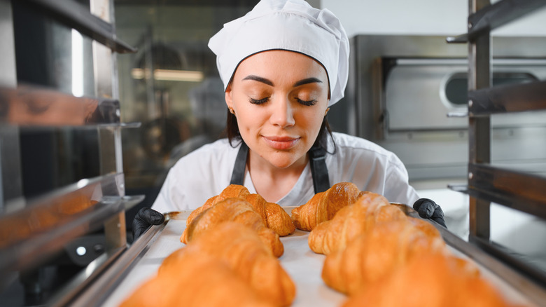 A baker smelling with closed eyes the aroma of freshly baked croissants placed on a tray in a bakery