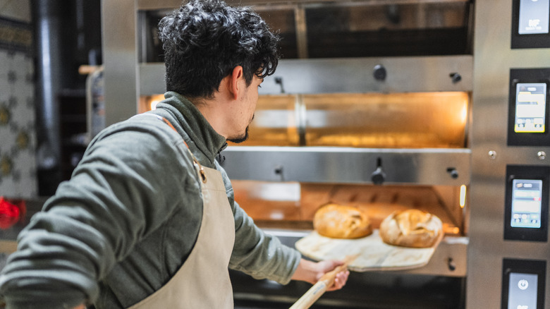 A baker removing two loaves of freshly baked bread from a professional oven