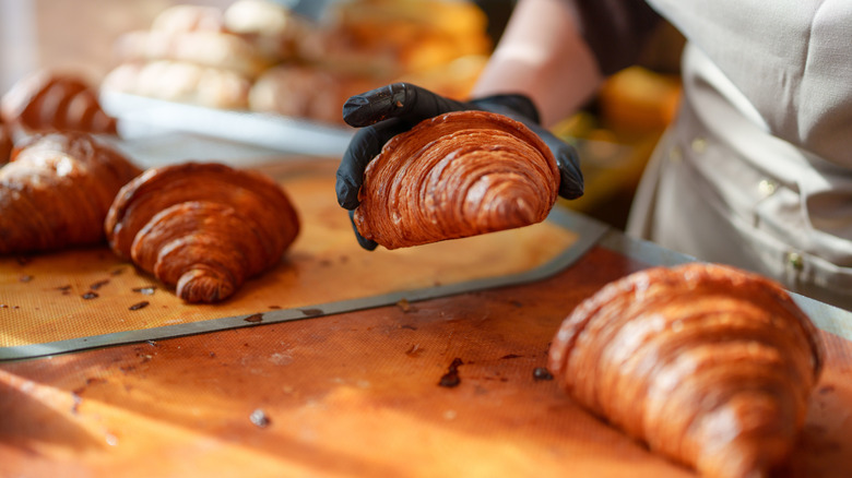 Close-up of a baker's gloved hands setting croissants onto a counter