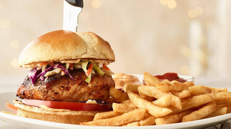 Bonefish Grill fish sandwich with knife stuck in top, with fries.