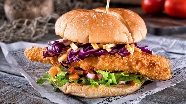 A fried fish sandwich with onion, French fries, red cabbage, lettuce & tomatoes.