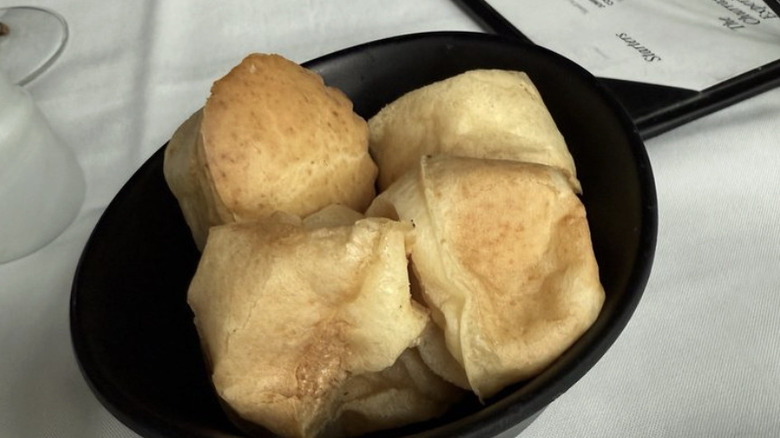 Four Fogo de Chao Pao de Queijo in black dish on white tablecloth