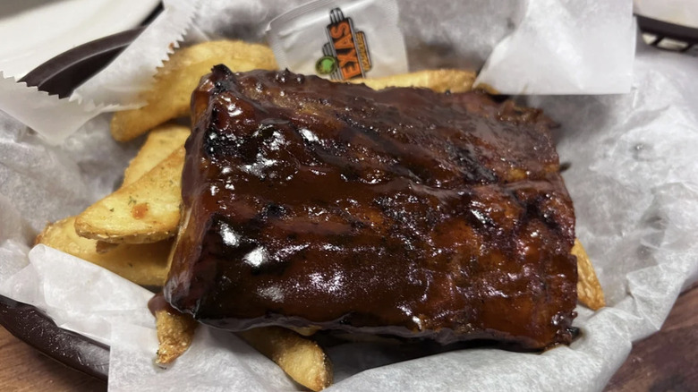 Texas Roadhouse ribs on top of french fries in a dish with white paper
