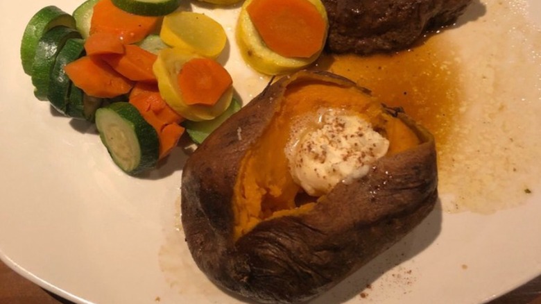 Outback Baked Sweet Potato with butter and brown sugar on white plate with mixed veggies