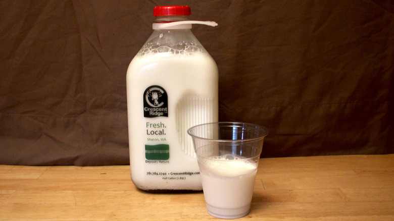 A glass jug of Crescent Ridge brand whole milk beside a cup of milk