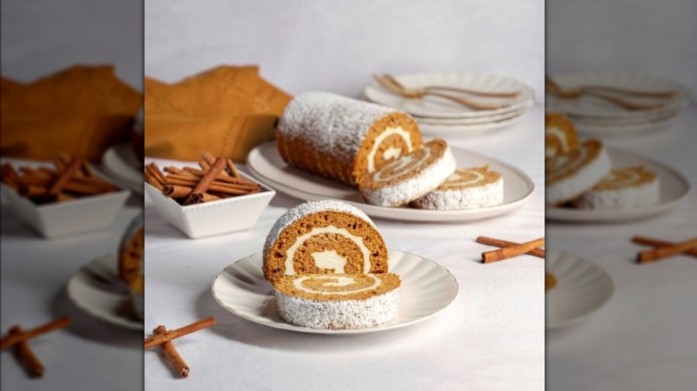 Pumpkin Cake Roll from Dutch Apron Bakery on a white plate with cinnamon and rustic decorations around.