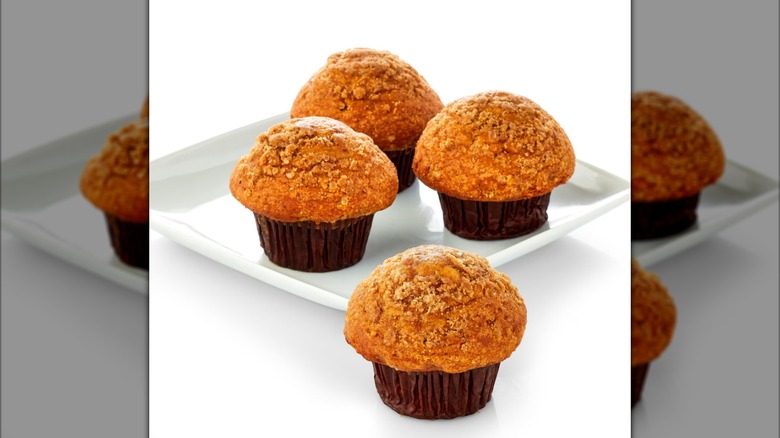 Four pumpkin muffins on a plate on a white background.