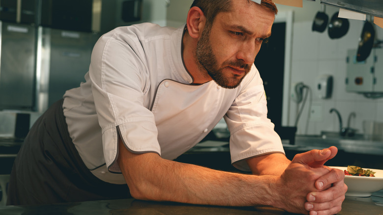 Tired and upset chef leaning on the pass in a restaurant kitchen