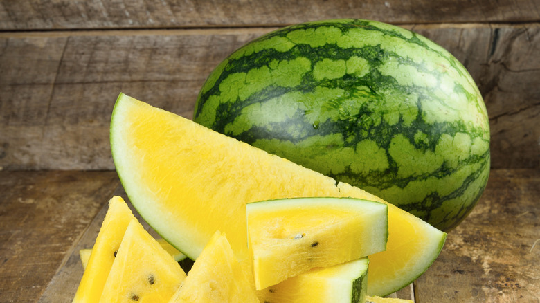Whole and sliced watermelon with yellow flesh on a wood table