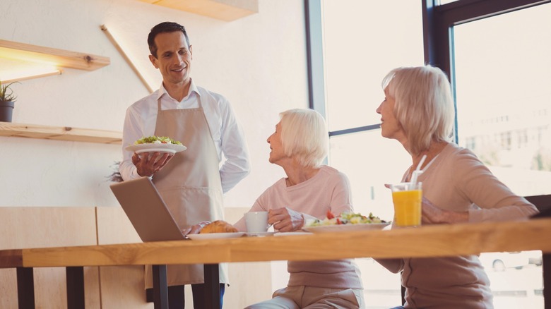 Waiter serving a salad to two women sat in a cafe