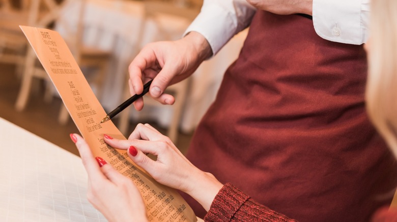 Cropped image of customer looking and pointing at menu while asking waiter about food in menu