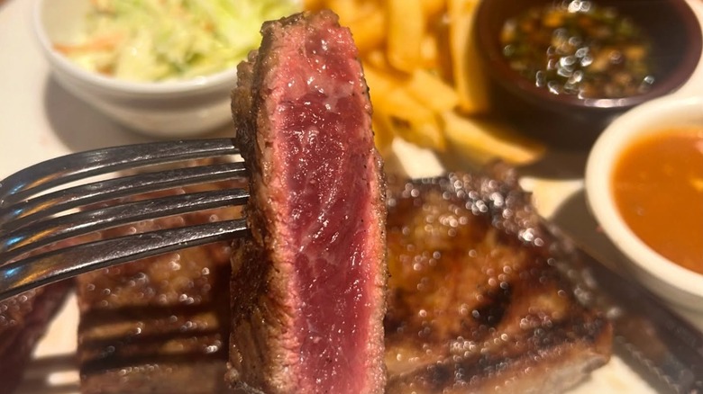 A piece of cooked steak held up by a fork in front of a plate of food.