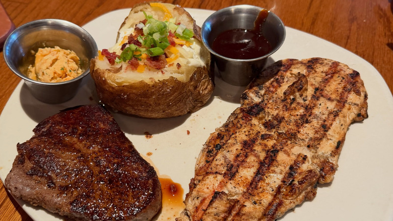 A plate of Outback Steakhouse food: a steak, grilled chicken breast and loaded baked potato.