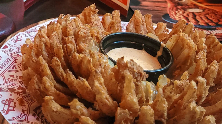 A large plate filled with a Bloomin' Onion side, made from a large fried onion with a container of sauce inside.