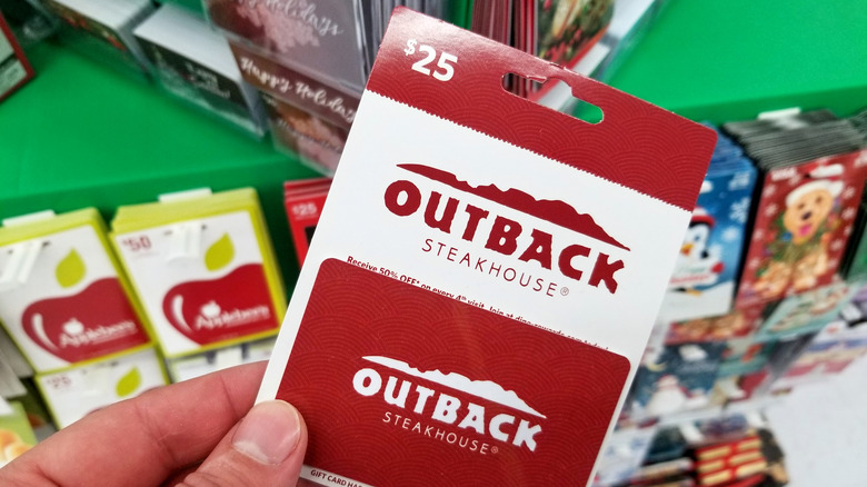 A hand holding an Outback Steakhouse gift card in the middle of a big box store