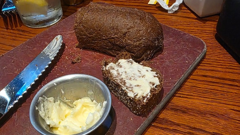 A plate with Outback Steakhouse Honey Wheat Bread, next to a knife and a ramekin of butter