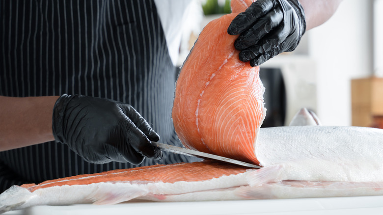 Gloved fishmonger cutting into salmon