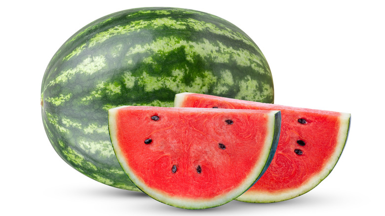 A whole watermelon with two slices in front of it on a white background