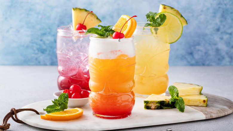 Three tiki-type drinks with orange, cherry, and pineapple garnishes